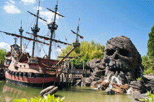 A pirate ship in the water near some rocks.